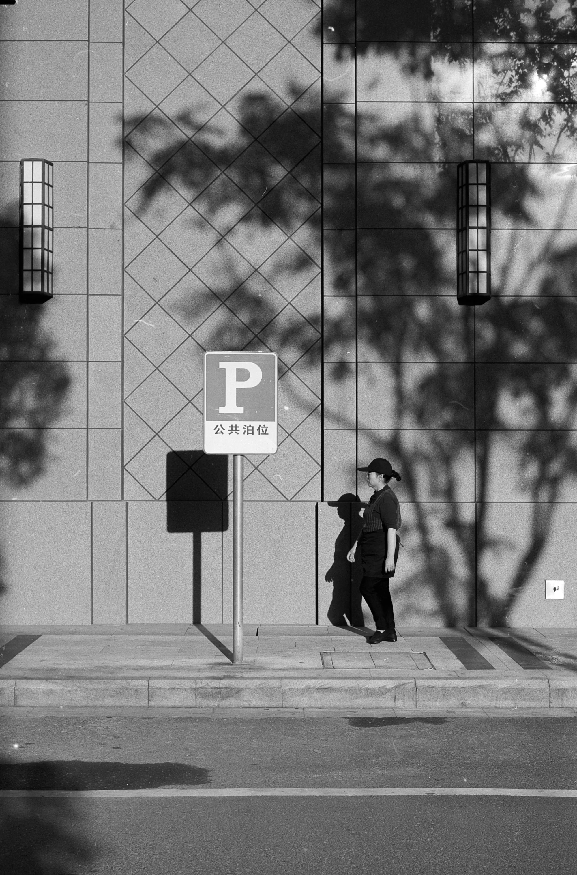 Two people walk beneath a parking sign against a large patterned building facade.