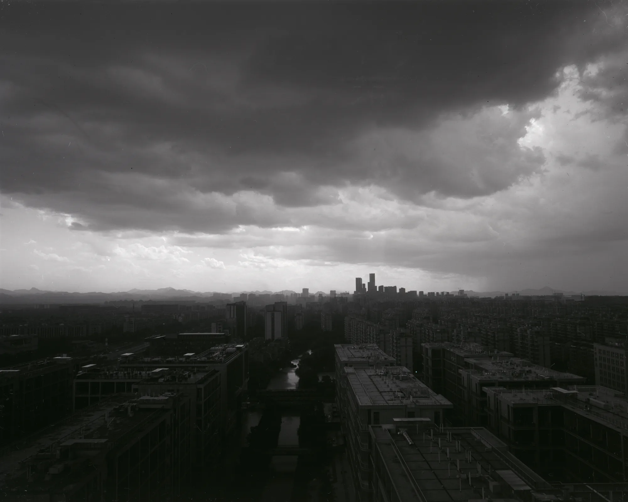 Heavy storm clouds gather over a distant city skyline and dark green fields.