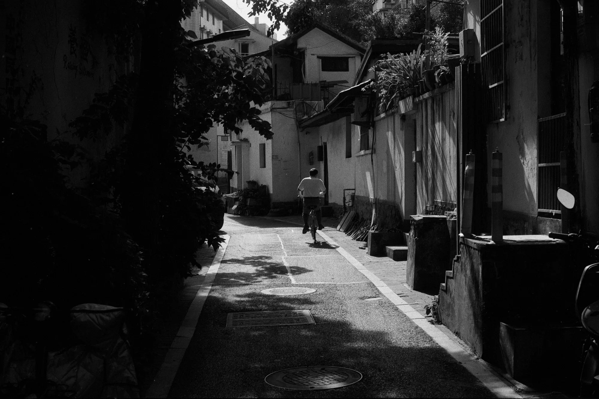 A narrow residential lane curves between old buildings beneath patches of tree shadow.