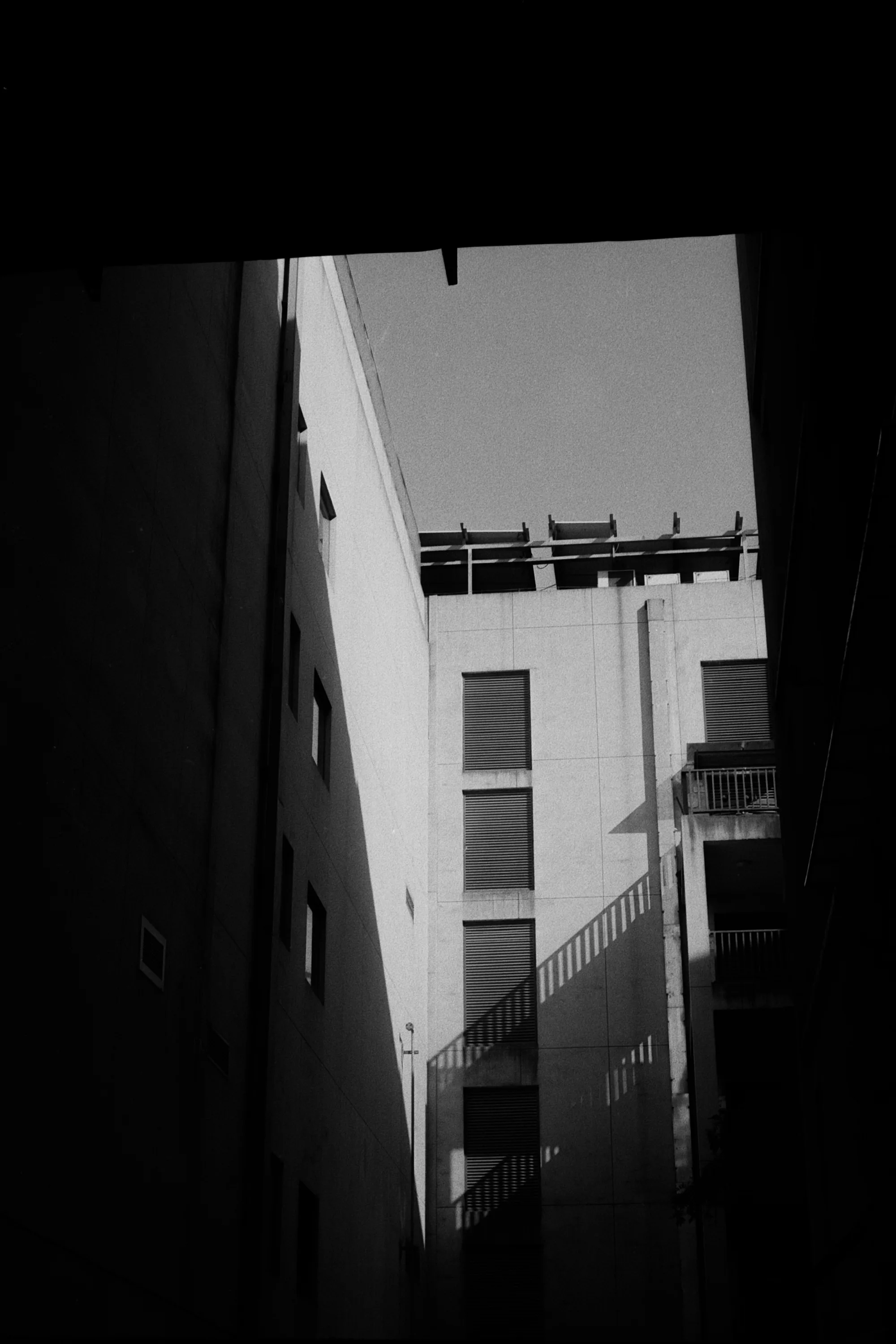 A bright white building and strip of sky appear through a narrow gap between dark walls.