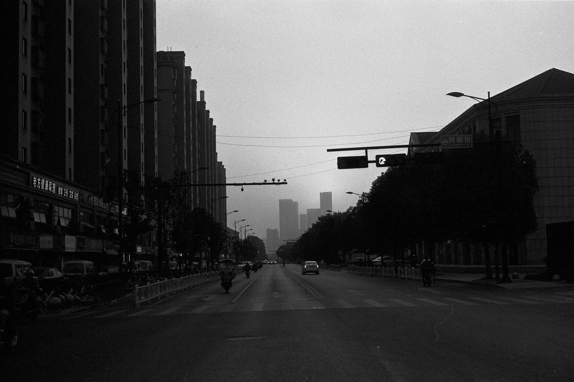 A wide city avenue stretches toward the horizon between dark rows of buildings and trees.