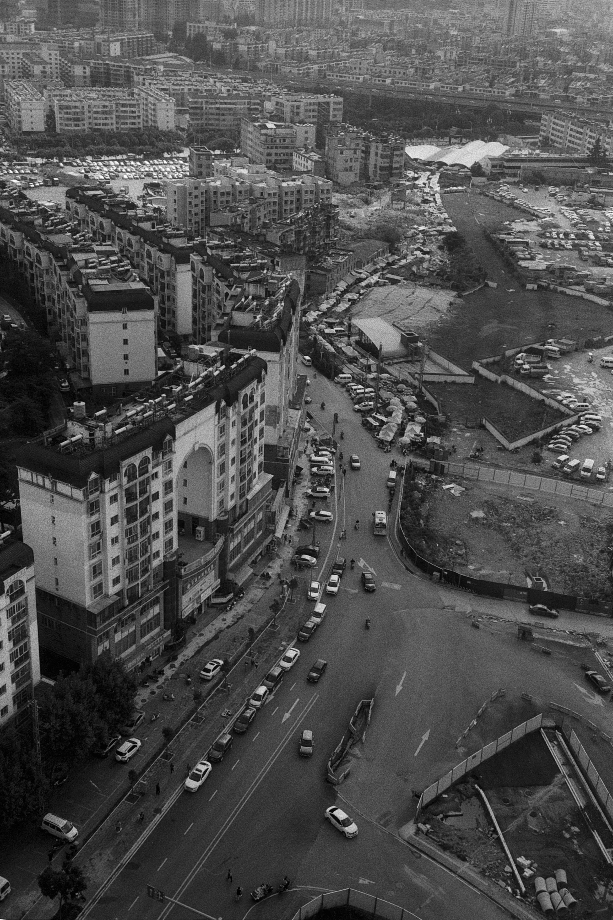 A high view looks down over curving roads, dense rooftops, and buildings in Kunming.