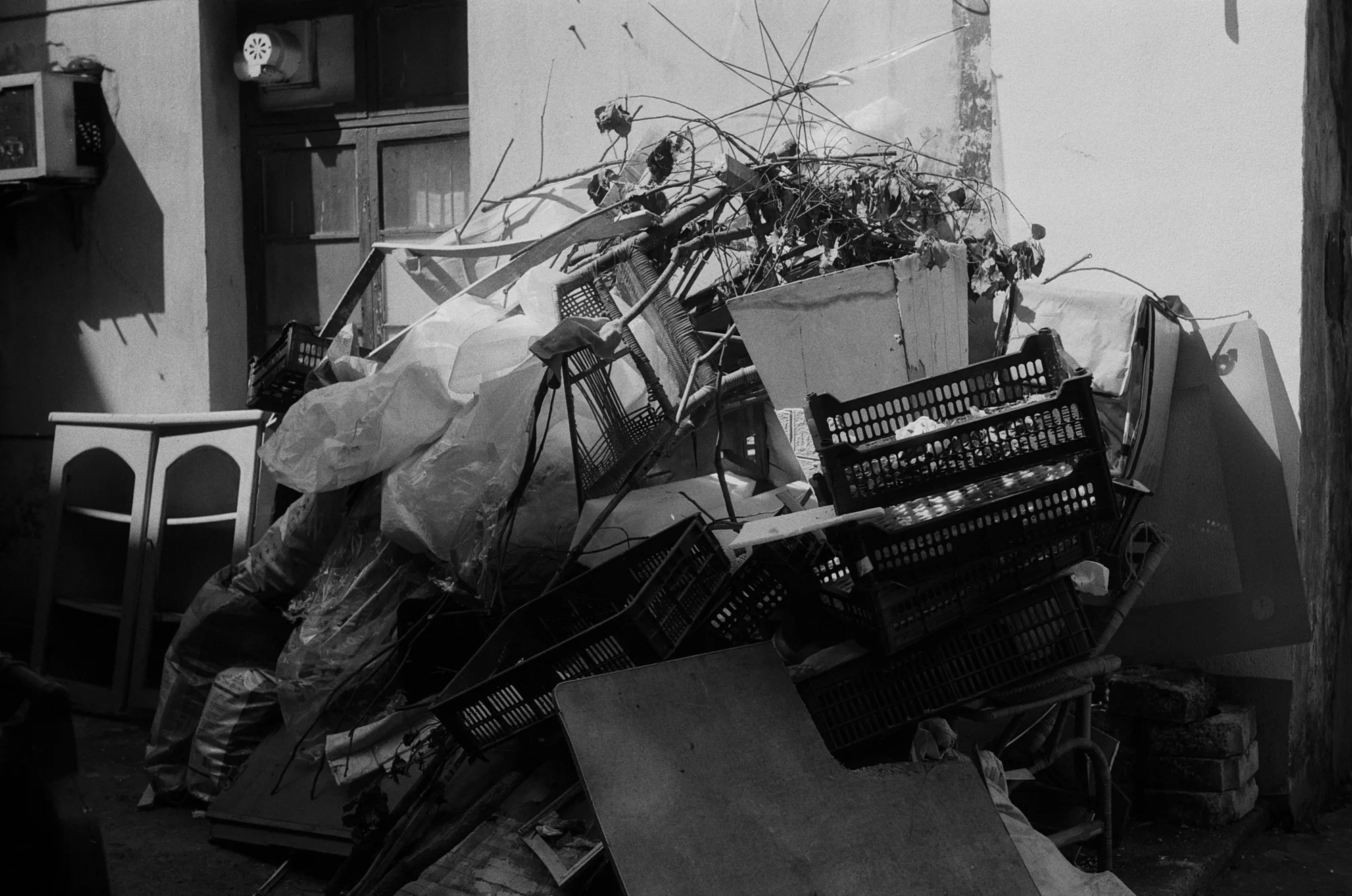 Bicycles, baskets, bags, and other objects are piled together against a wall.
