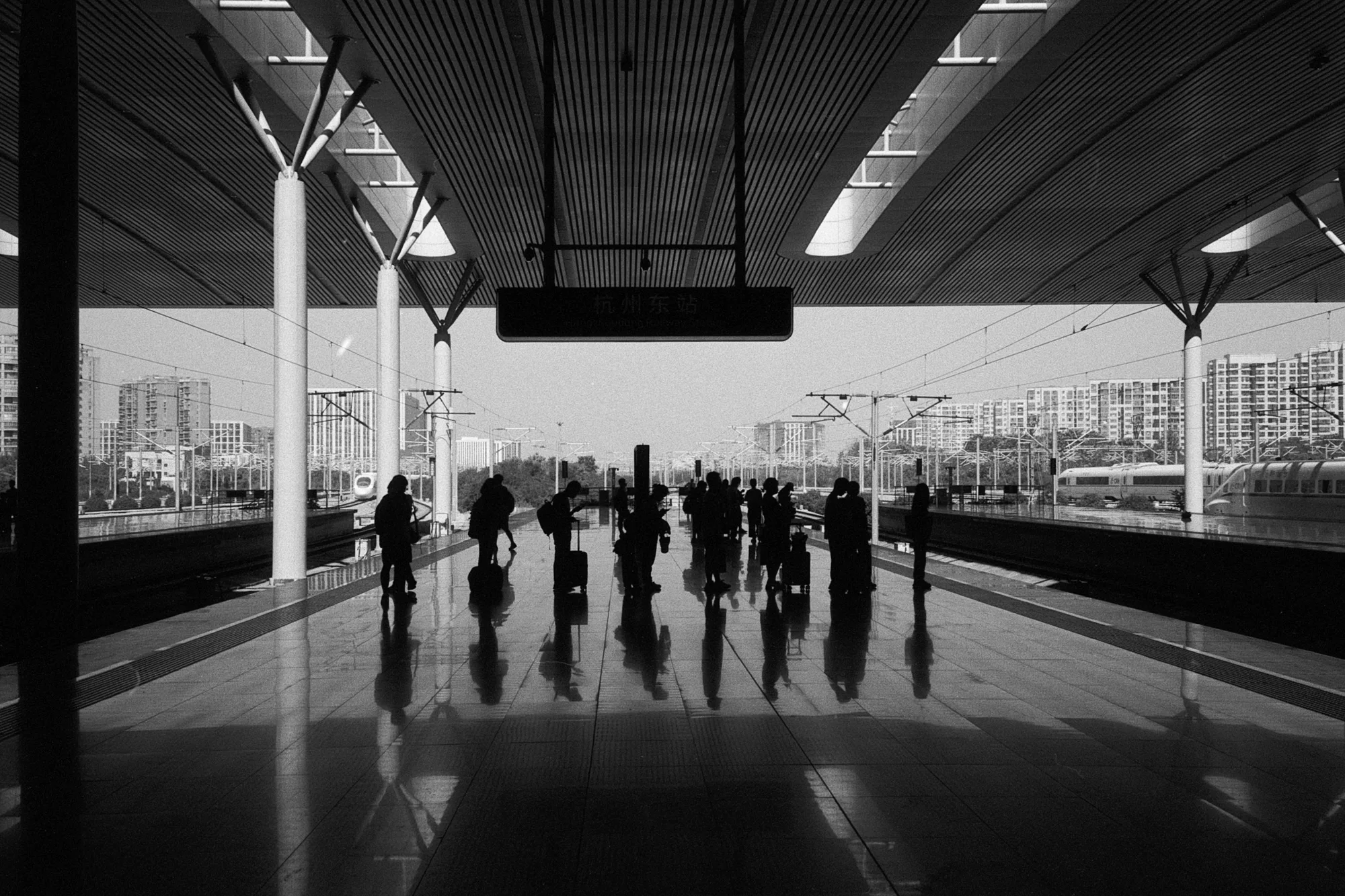 Passengers walk across a railway platform, their figures reflected on the polished floor.