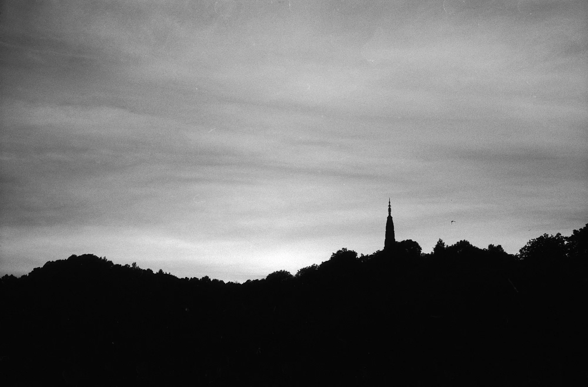A pointed tower breaks the silhouette of a dark hill beneath a streaked evening sky.