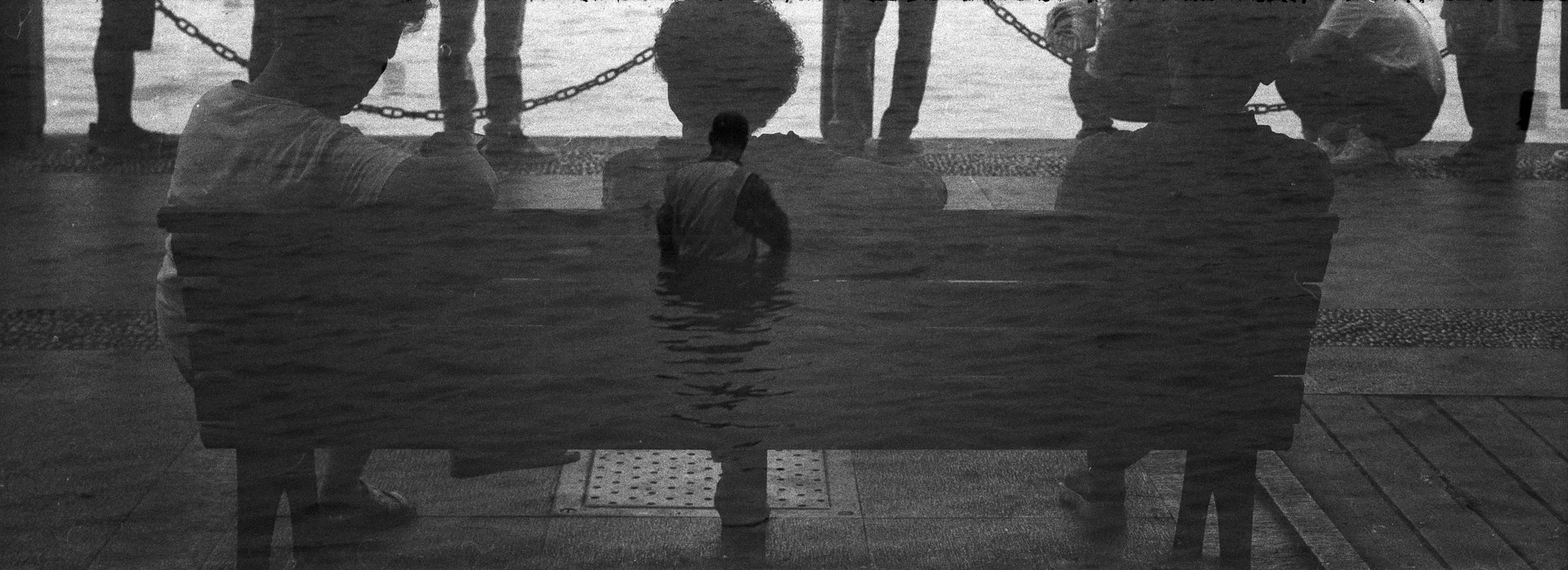 Dark figures standing by the water merge with their rippled reflections.