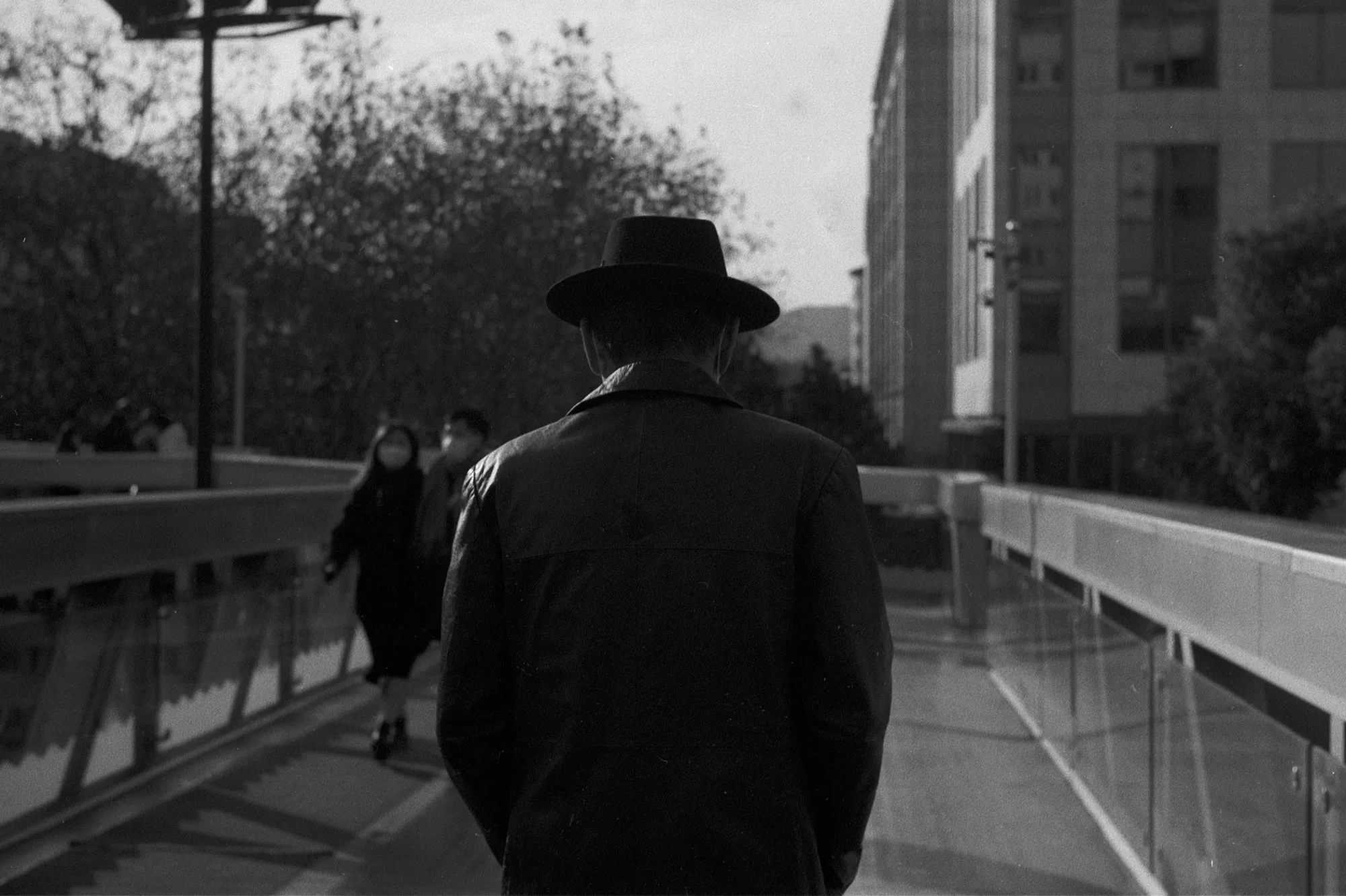 A person in a dark wide-brimmed hat walks away along a raised pedestrian path.