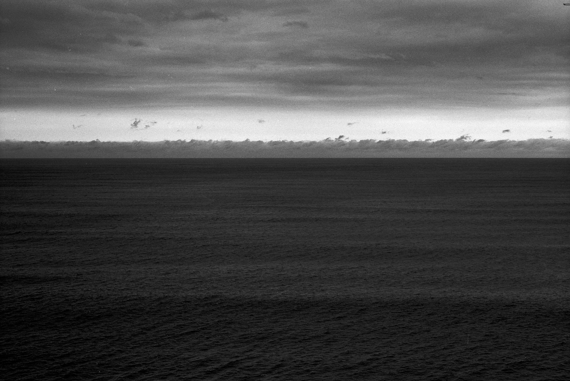 A dark, nearly empty sea extends toward a narrow bright horizon beneath heavy clouds.