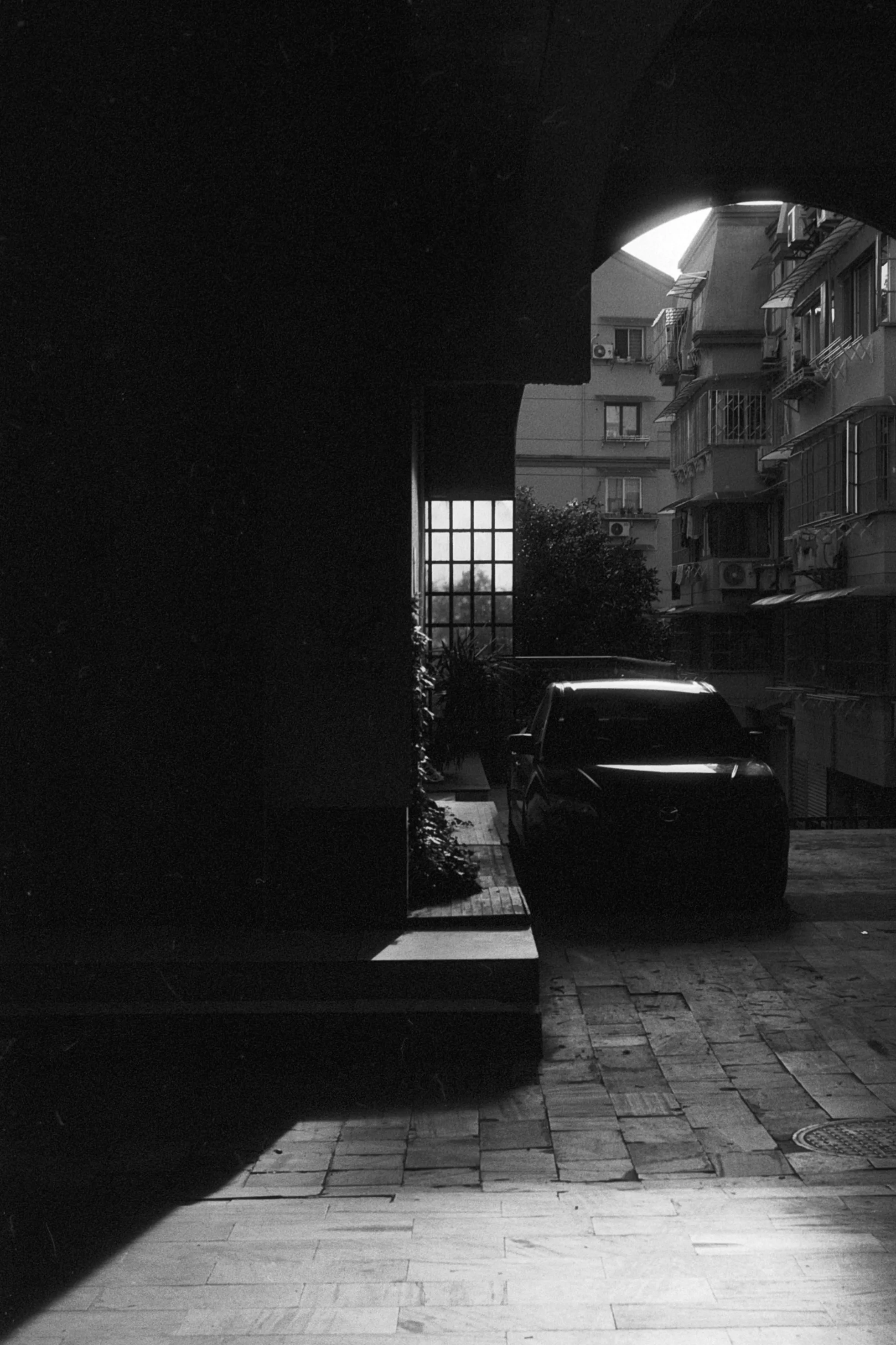 A parked car catches sunlight at the far end of a narrow alley framed by deep shadow.
