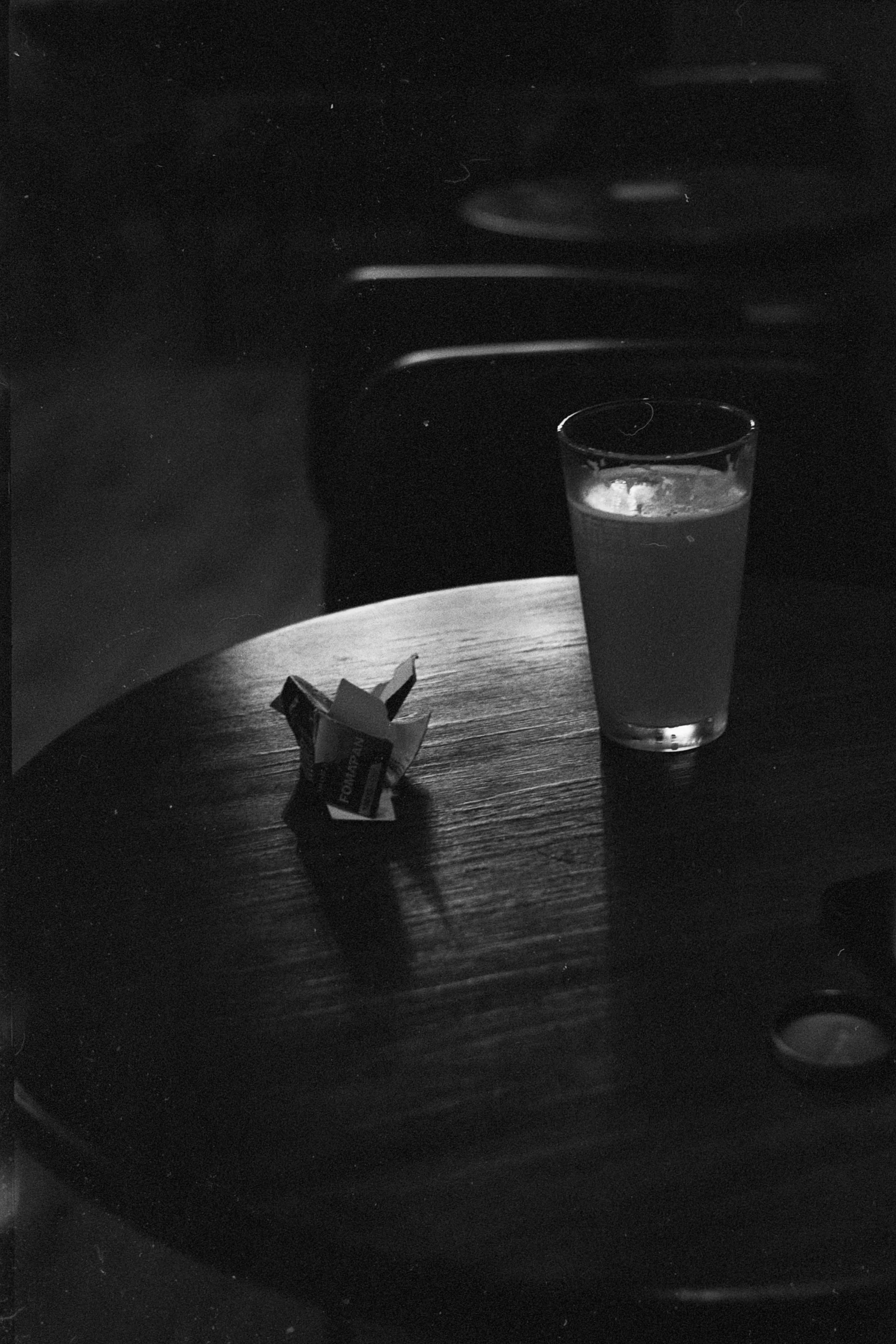 A single glass and folded napkins sit on a round table in a dark room.