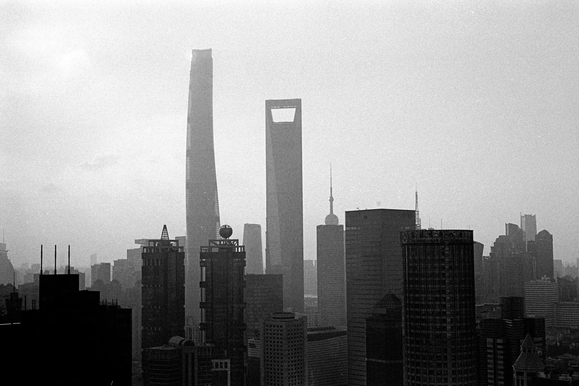 Shanghai's tall central towers rise above dark rooftops through a layer of haze.