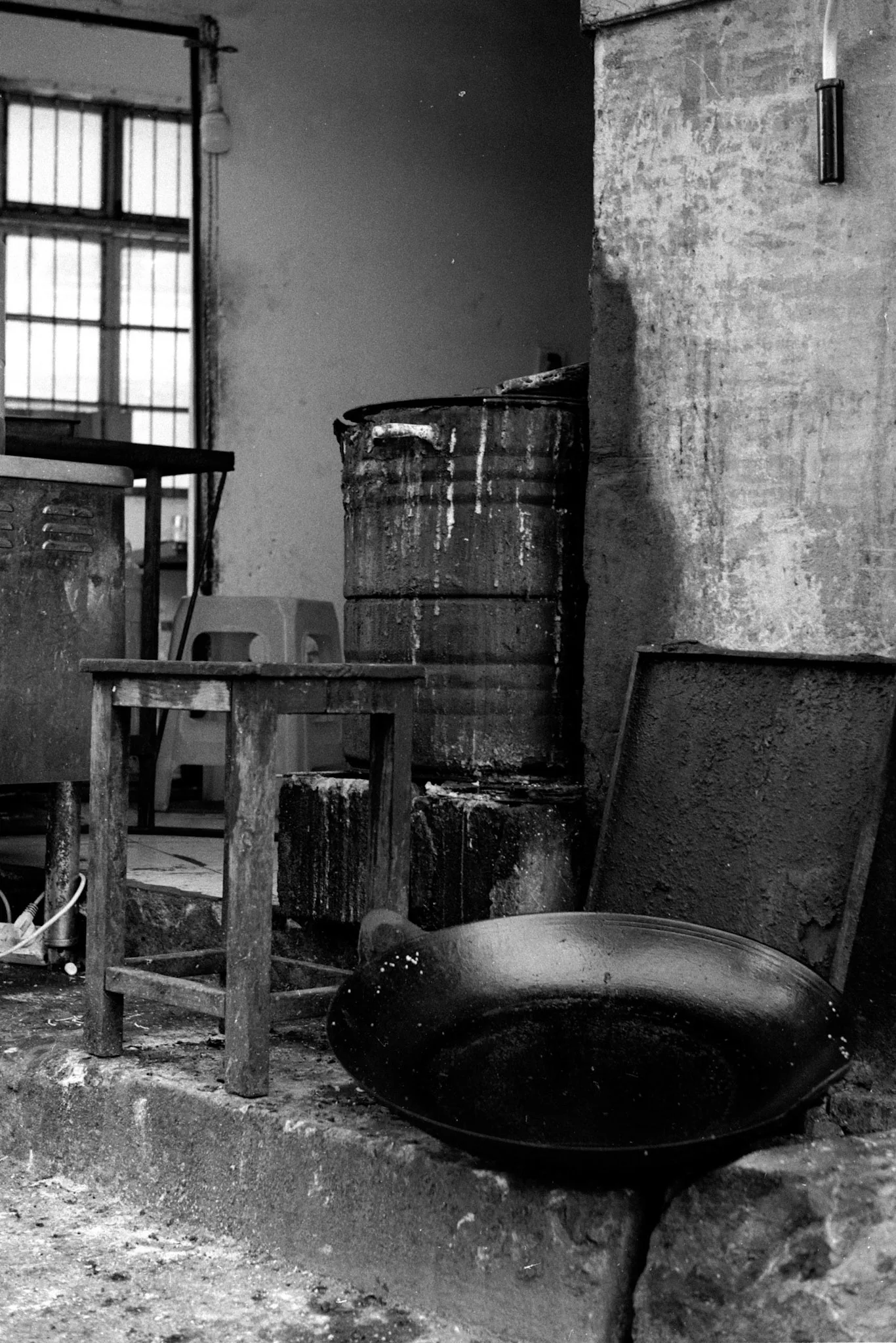 A worn chair and metal barrel sit inside a dusty, empty industrial room.