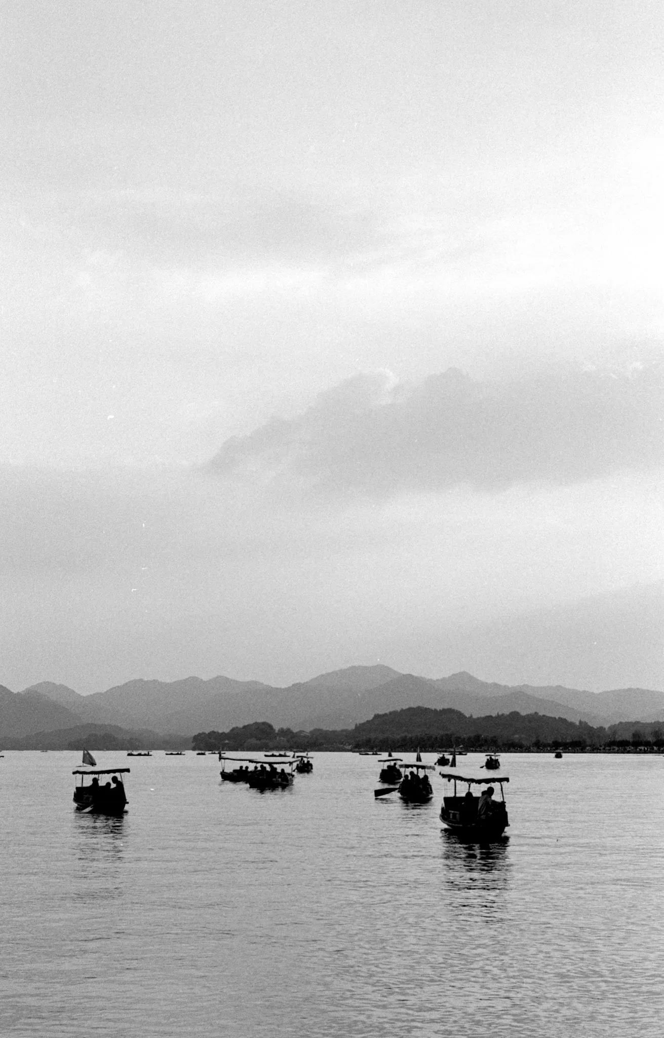 Several small boats float on West Lake with layered hills fading into the distance.