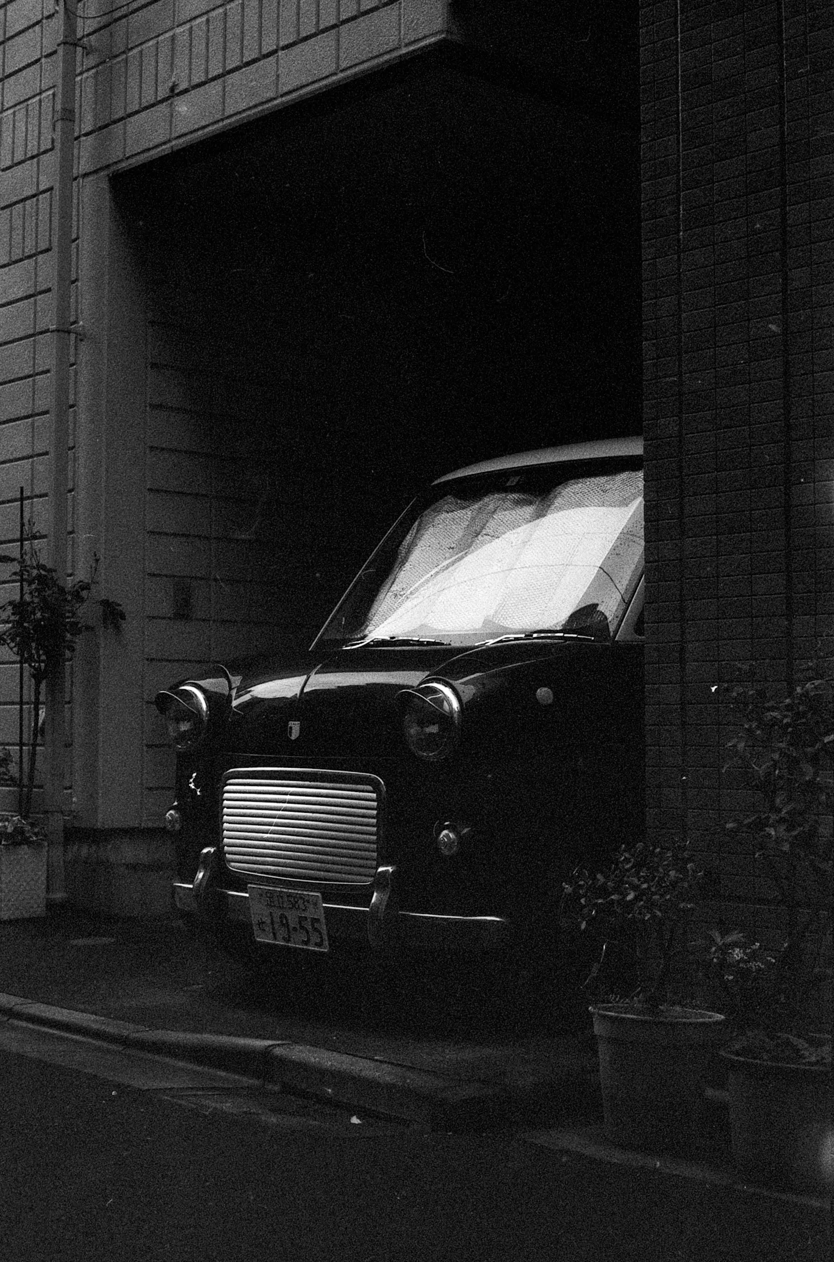 A black taxi sits partly hidden in the deep shadow beneath a modern building.