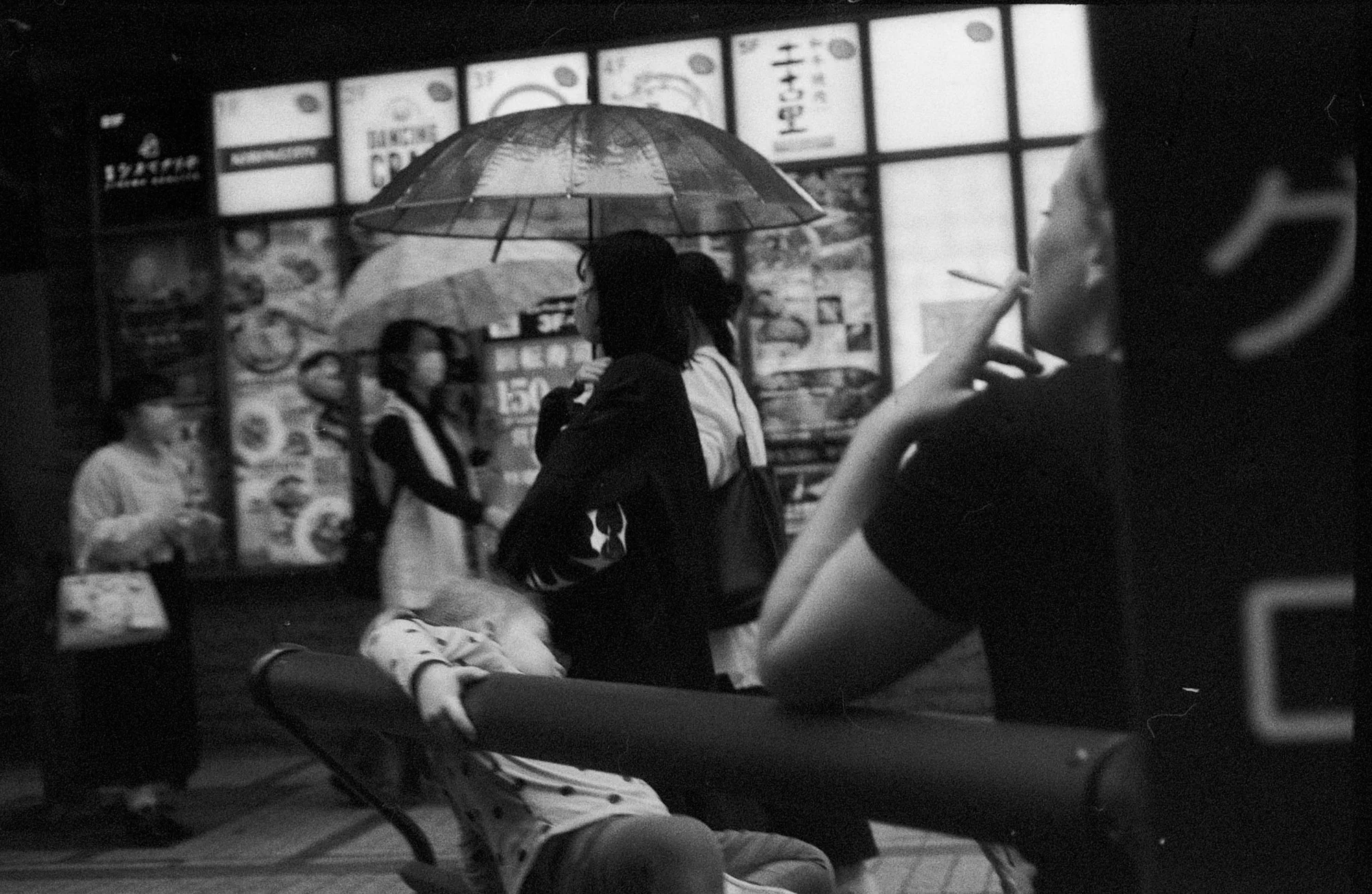 Cyclists wait near a busy crossing while a dark umbrella fills the foreground.