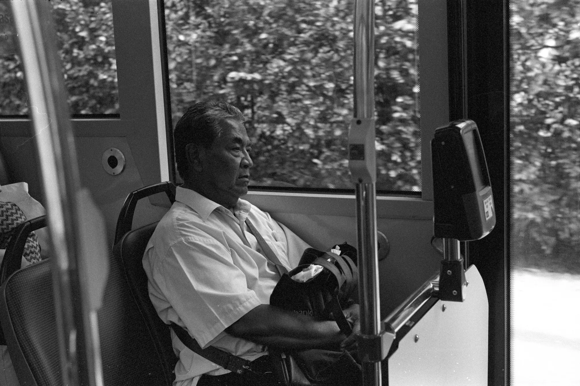 A passenger sits beside a bus window with one hand resting on a bag.