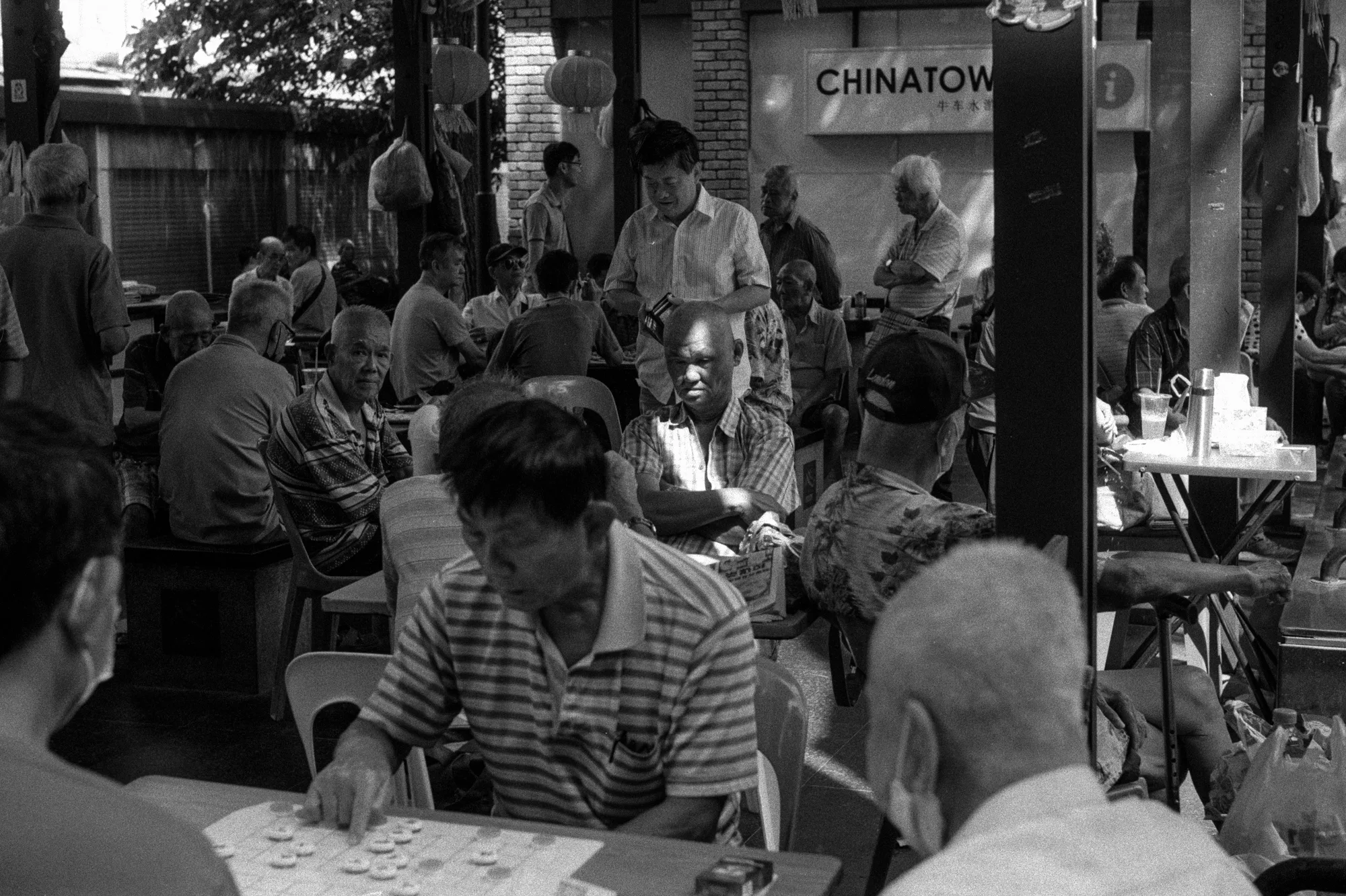 A crowd leans in around a table to watch a street game in Chinatown.