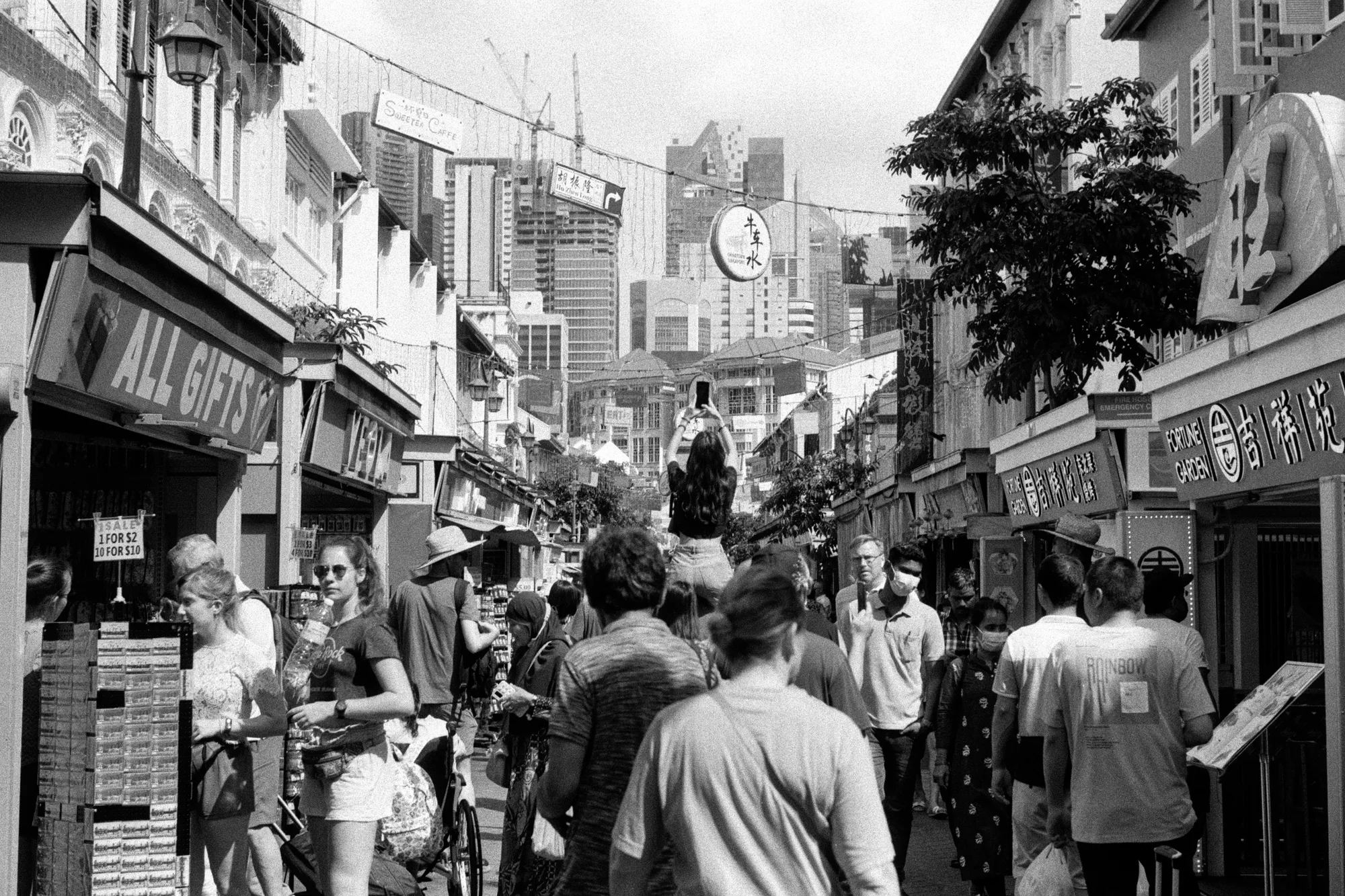 A dense crowd moves along a narrow Chinatown street between market stalls.