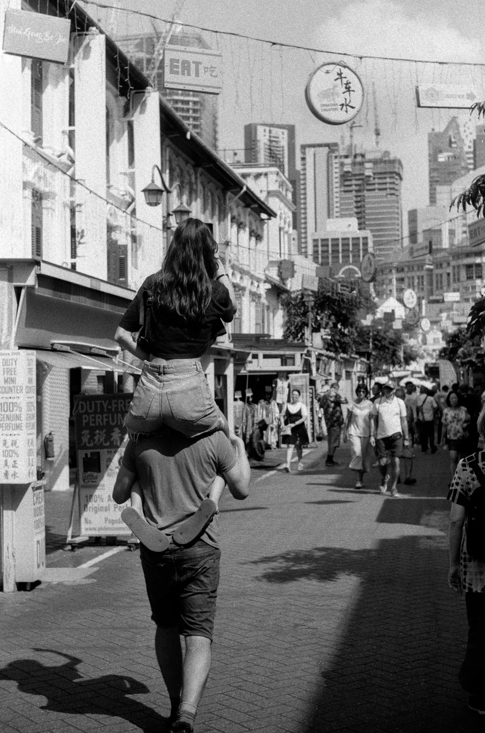 An adult walks down a Chinatown street carrying a child on their shoulders.