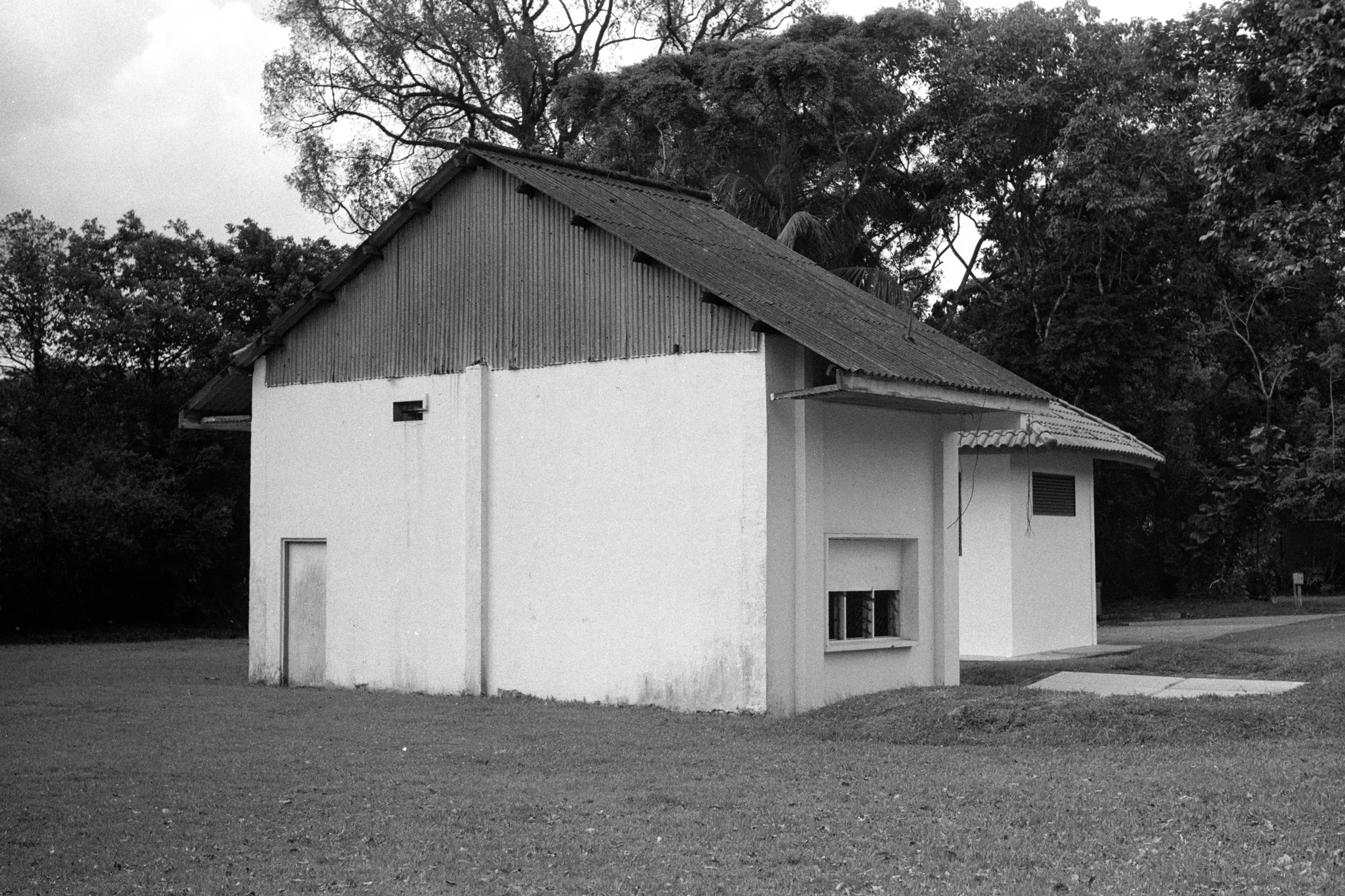 A small white building with a pitched roof stands alone on a broad grassy plot.