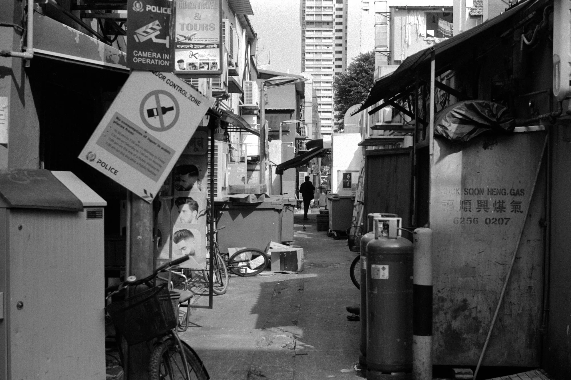 A quiet service lane is lined with bins, signs, bicycles, and the backs of shophouses.