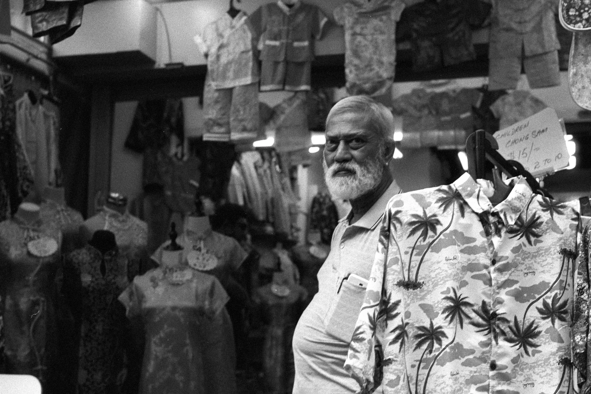 A bearded man wearing a palm-print shirt walks through a crowded Chinatown street.