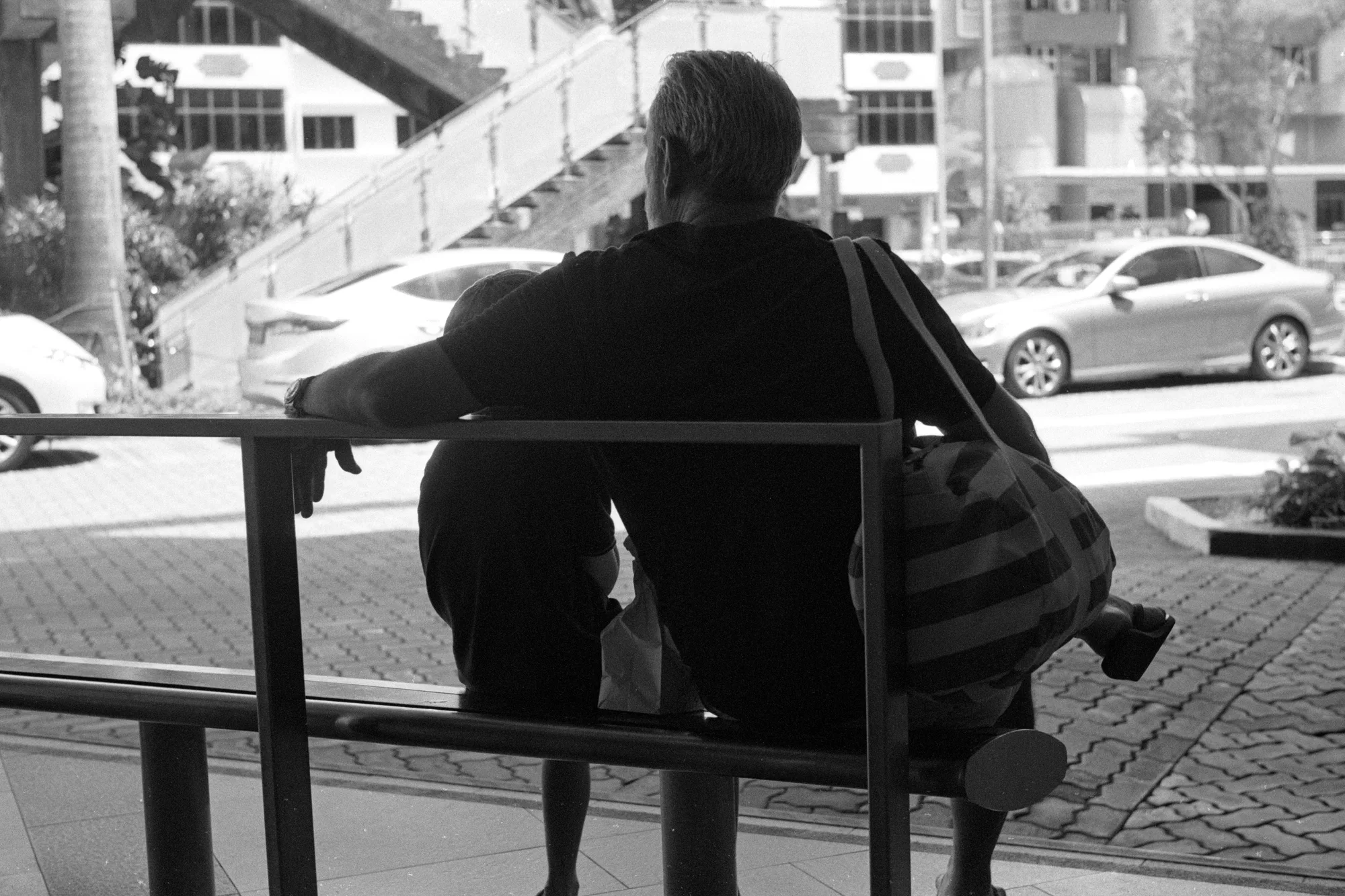 A seated adult with a large shoulder bag waits with their back to the camera.