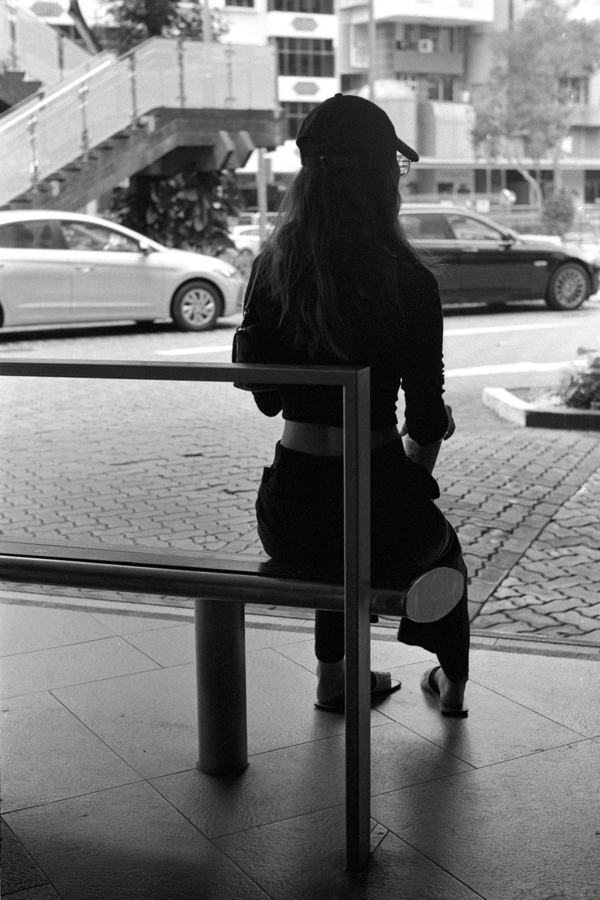 A person sits alone on the bus stop bench with a bag beside them.