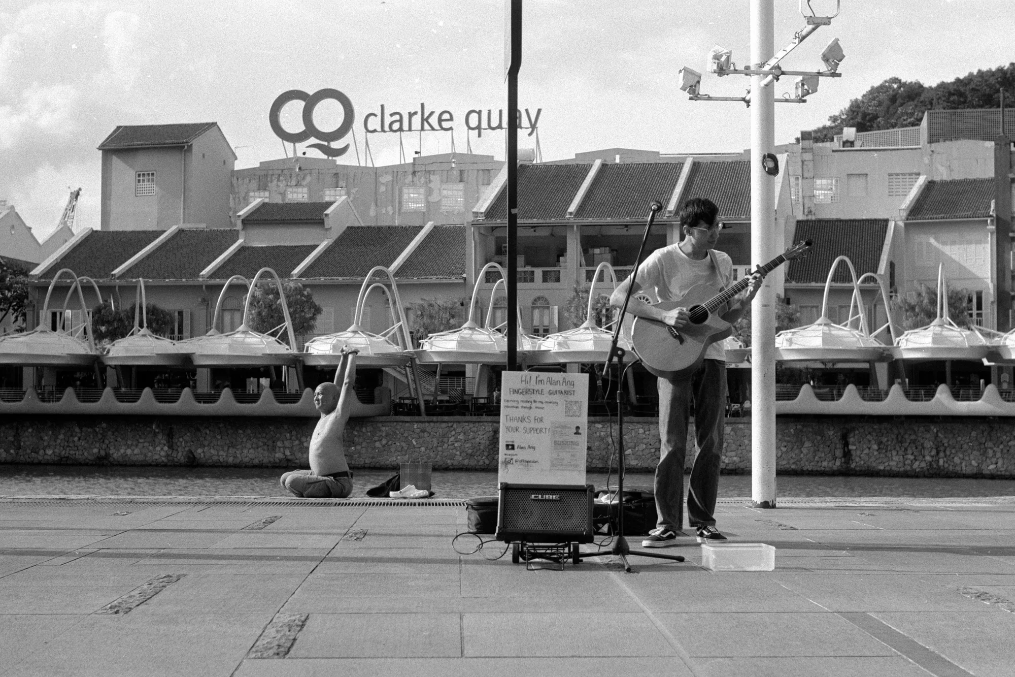 A guitarist sings into a microphone beside a small amplifier and open case.