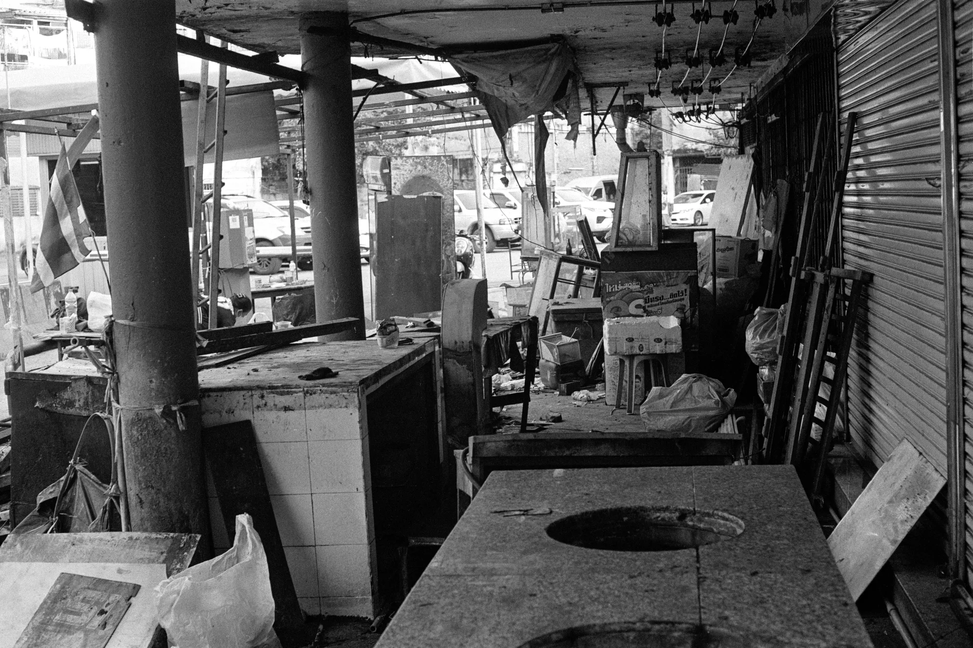 An empty cooking station and worn counters stand beneath the roof of a closed market.