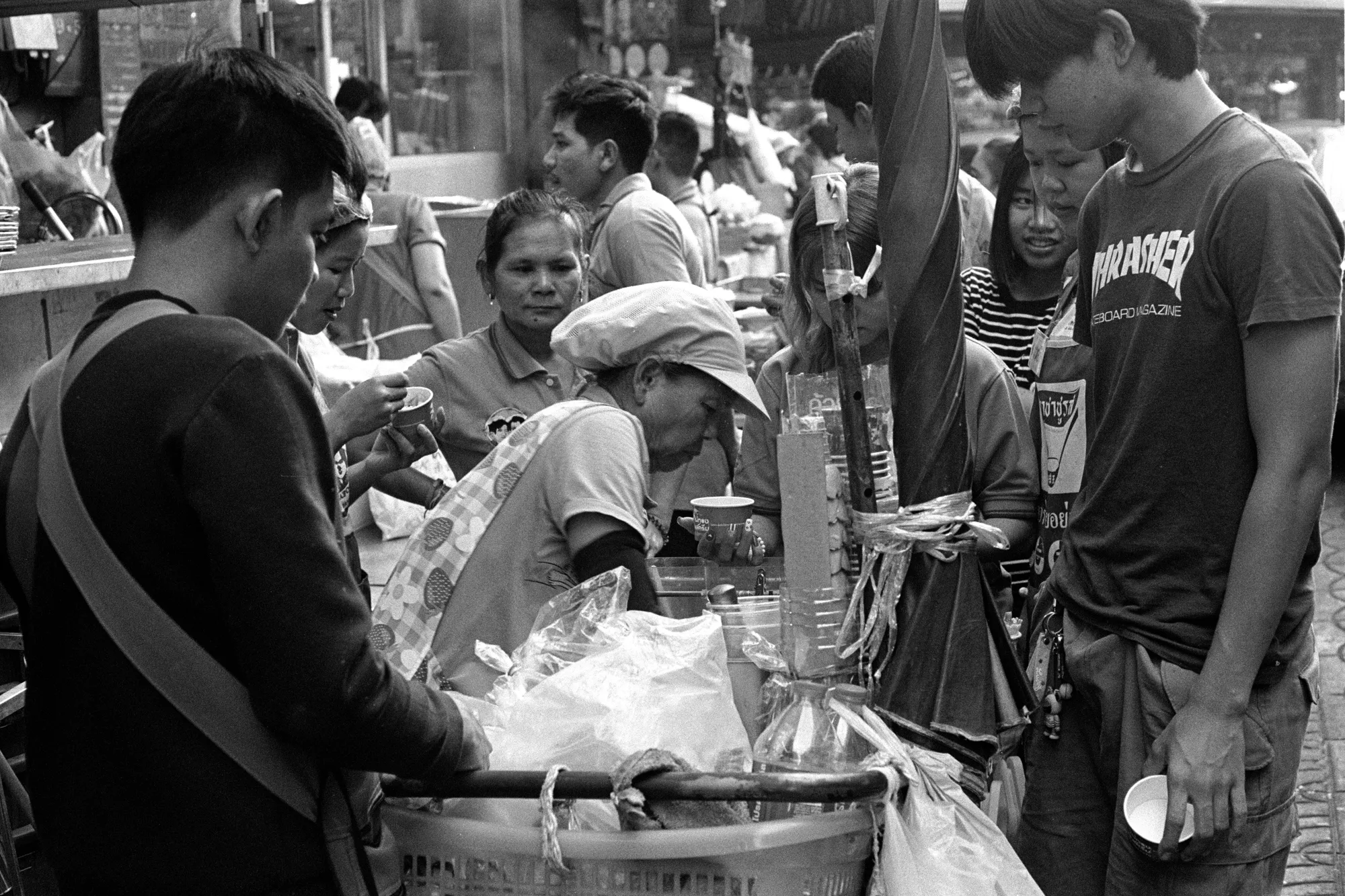 A small crowd gathers around a street ice cream cart while the vendor serves them.