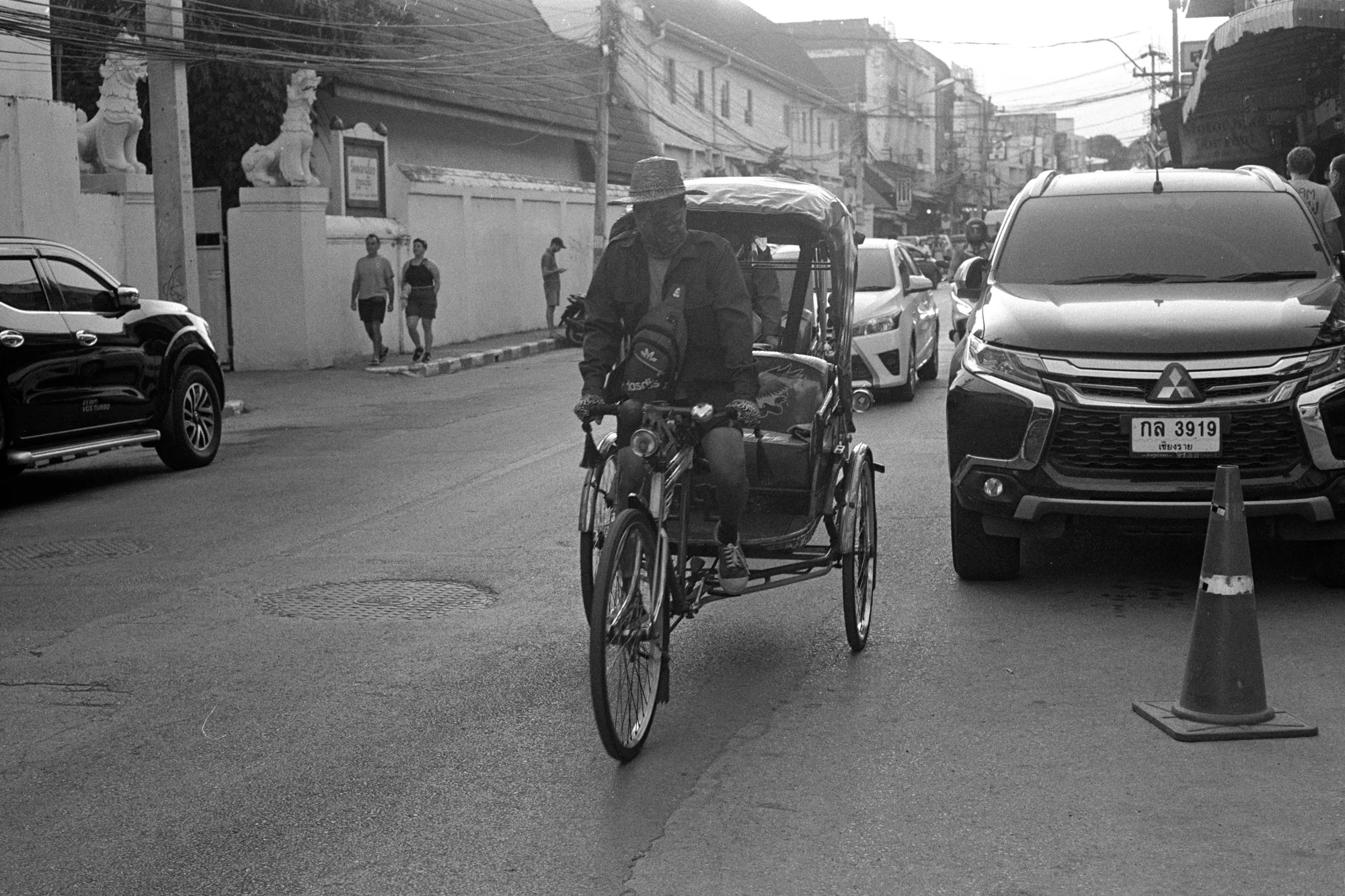 A pedicab rider travels between cars along a busy Bangkok street.