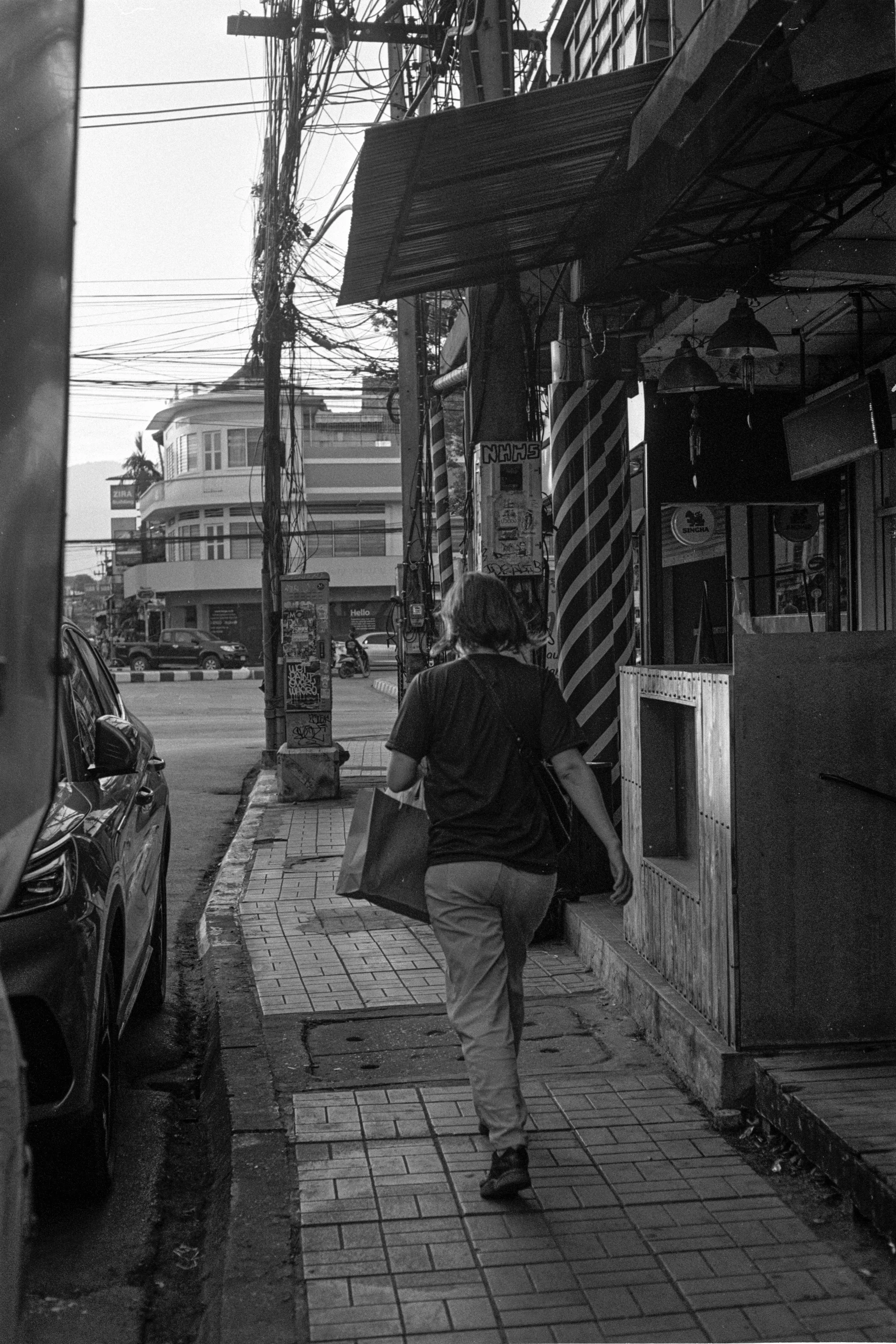 A person walks along a narrow lane lined with old buildings and utility wires.