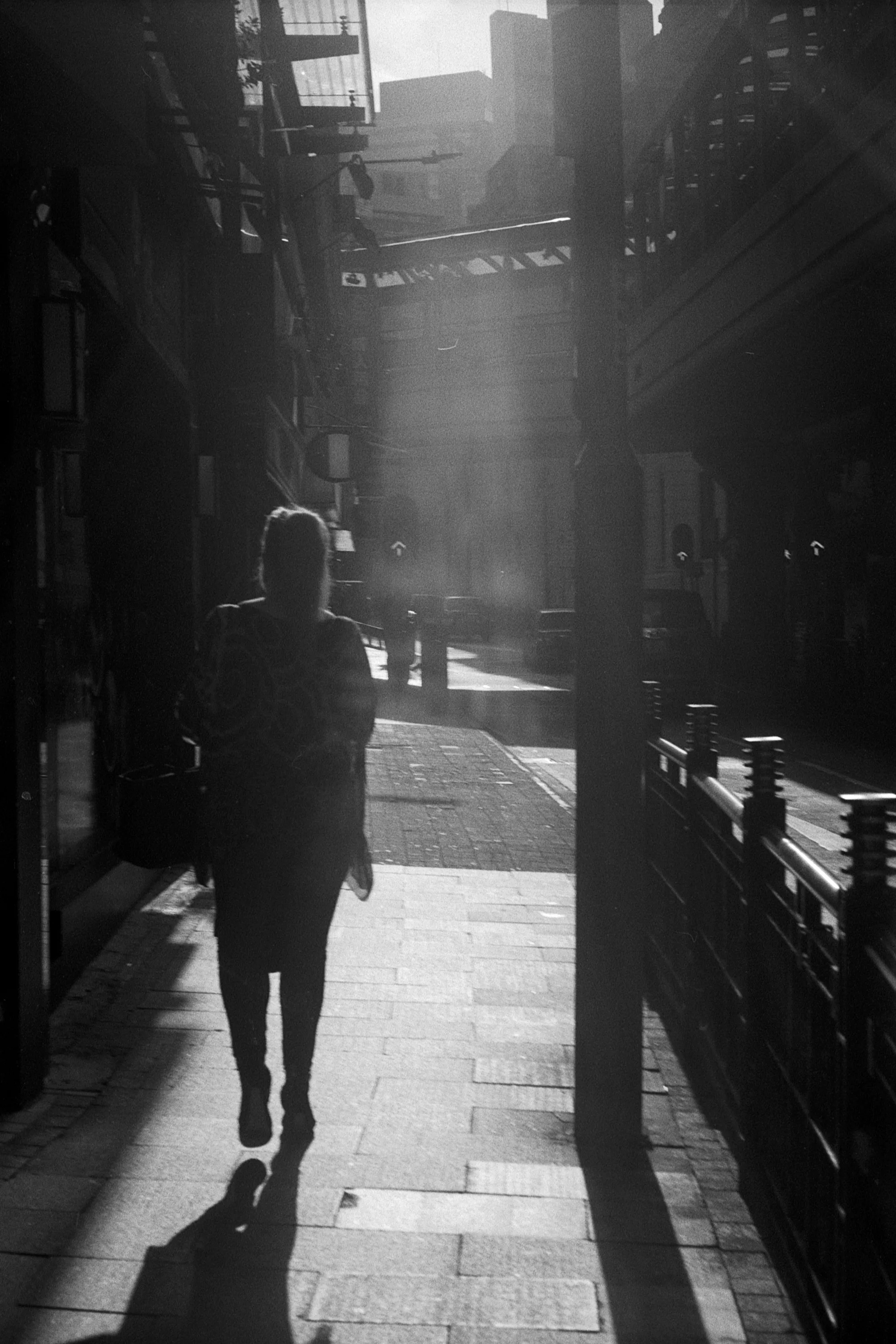 A lone figure walks through a narrow passage toward a bright rectangle of sunlight.