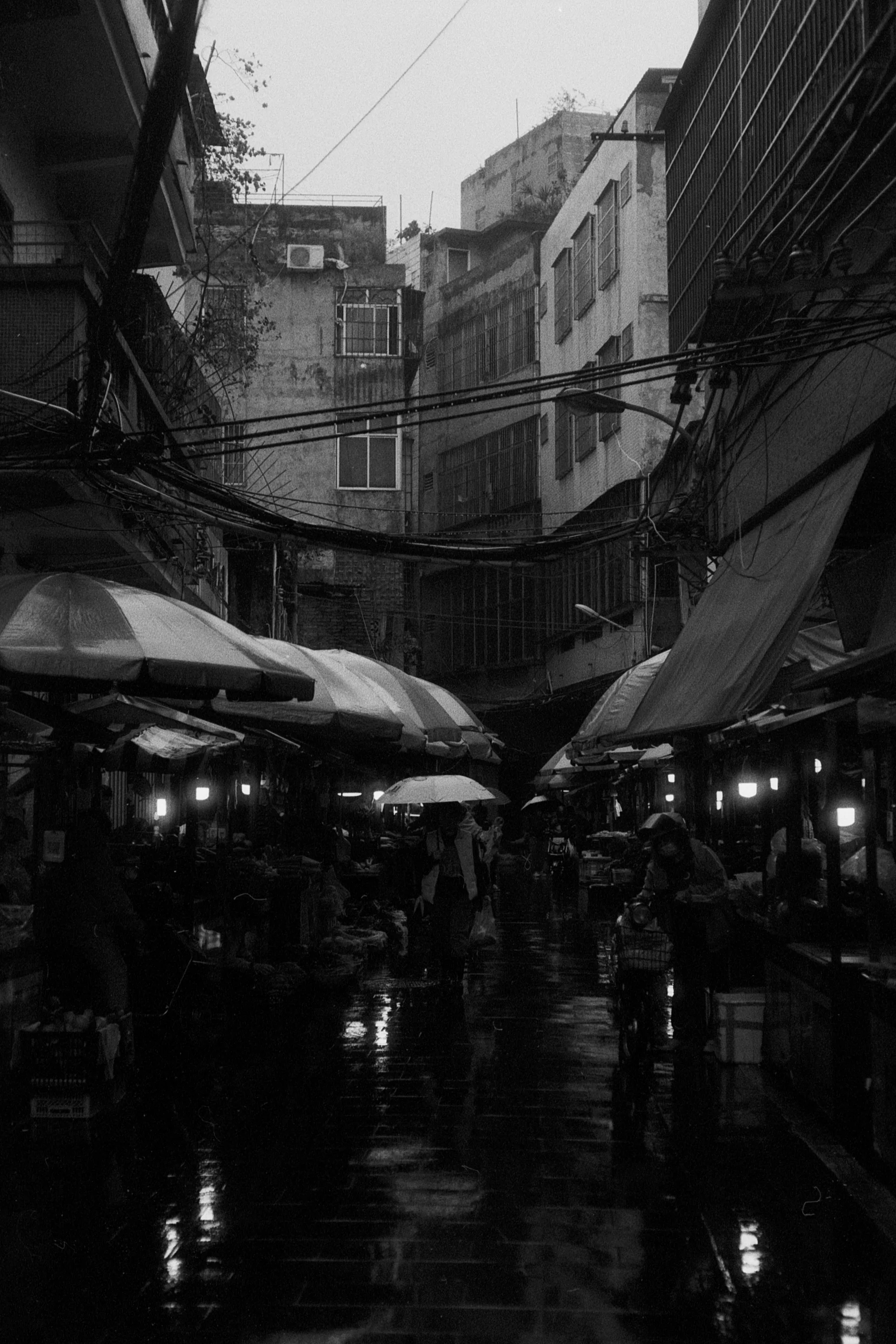 Market stalls and umbrellas line a wet lane between closely packed buildings.