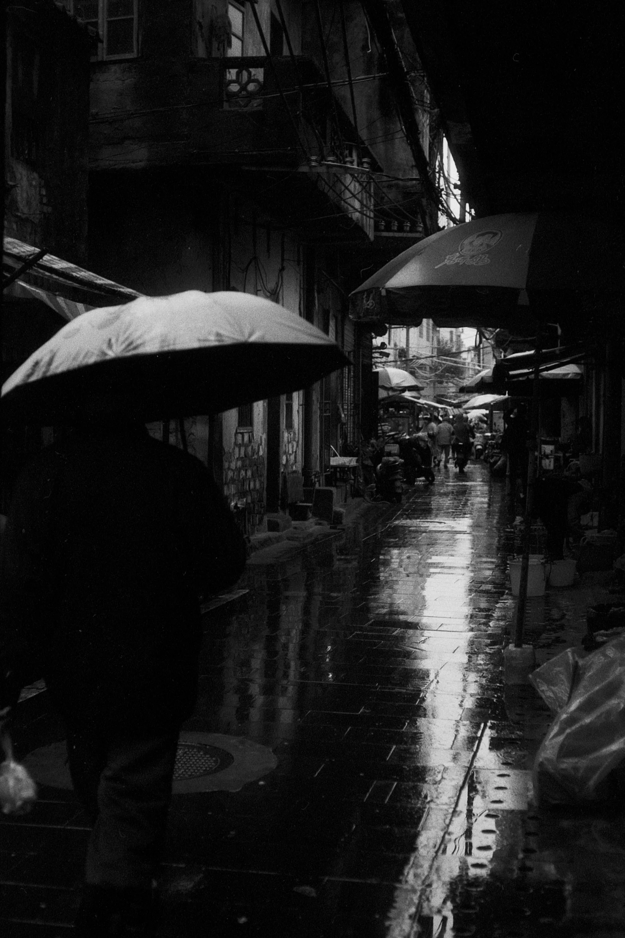 People carrying umbrellas walk through a dark fish market reflected in wet pavement.