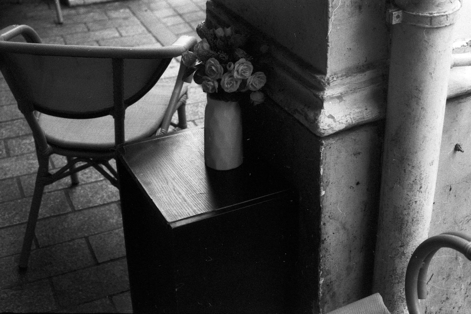 A bunch of flowers sits on a narrow ledge beside a metal pillar and an empty chair.
