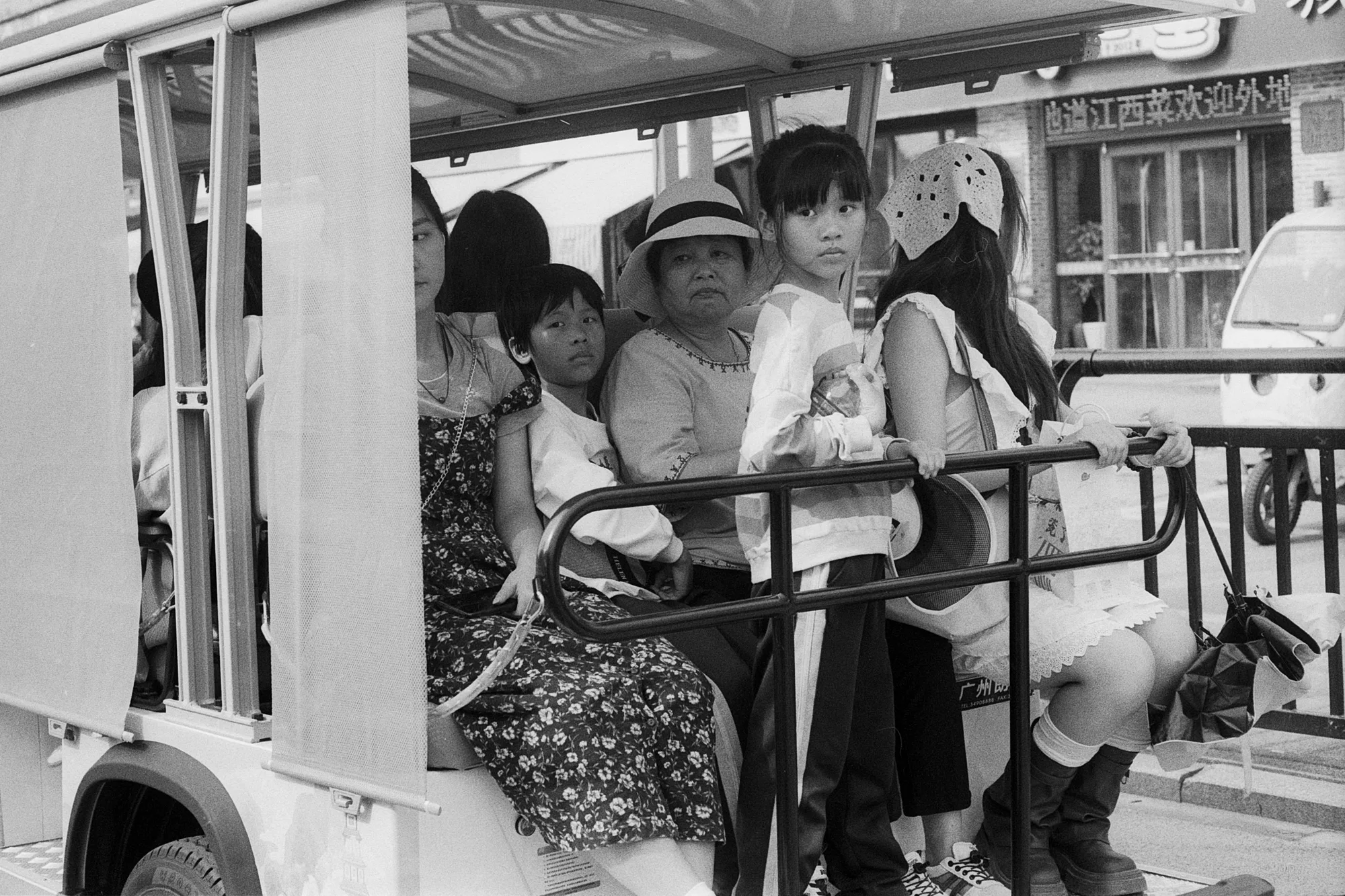 Several passengers sit closely together in the open back of a small shuttle.
