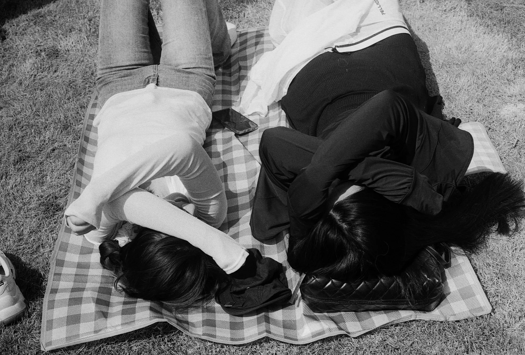 Two people lie face down side by side on a blanket spread over the grass.