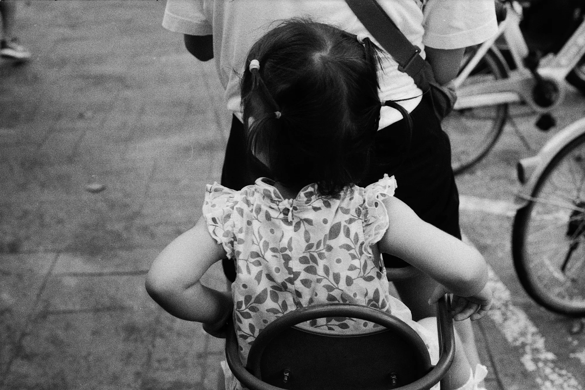 An adult bends toward a child sitting in a rear bicycle seat on a busy path.