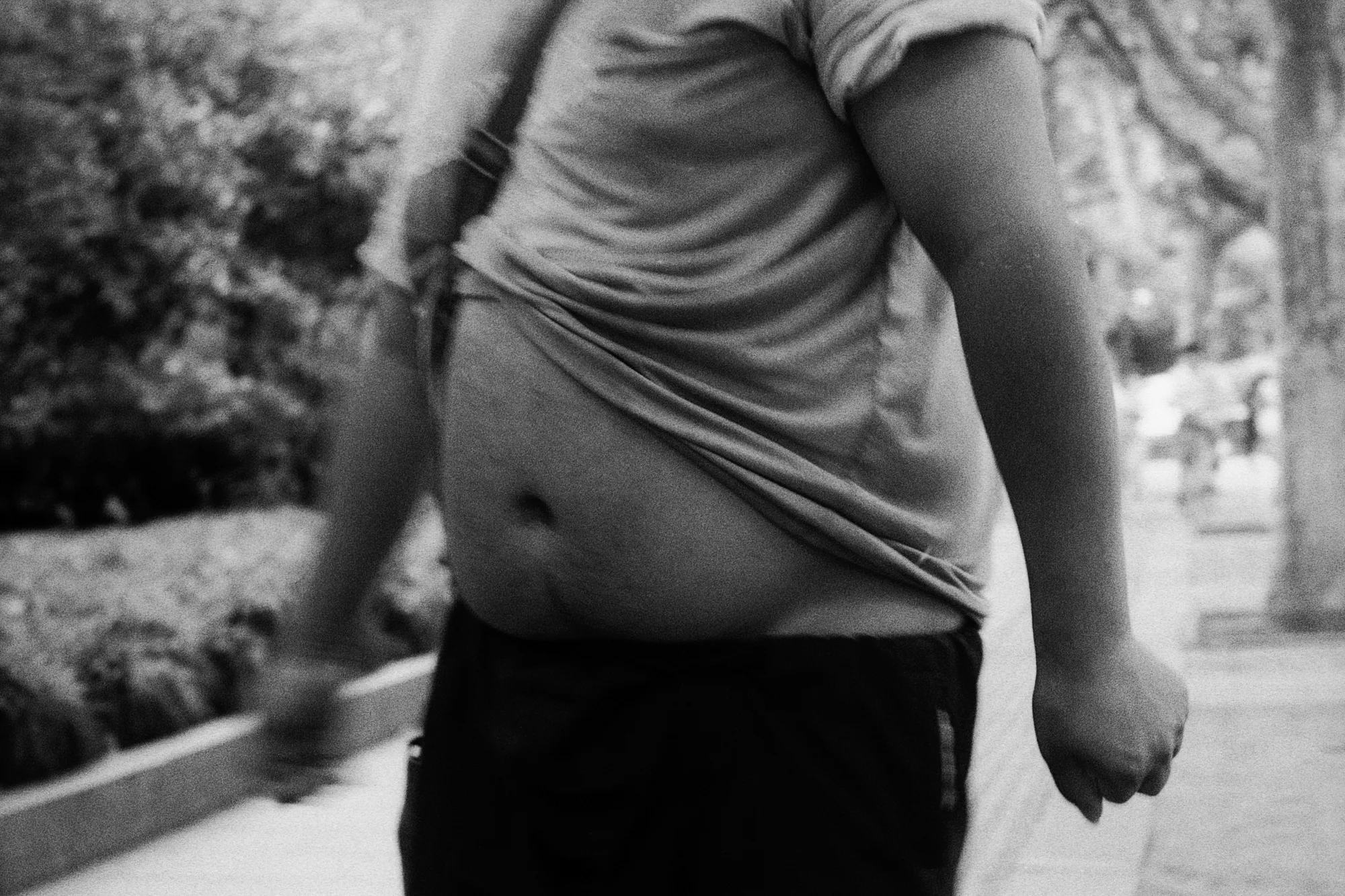 The torso and arm of a passerby fill the foreground of a tree-lined path.