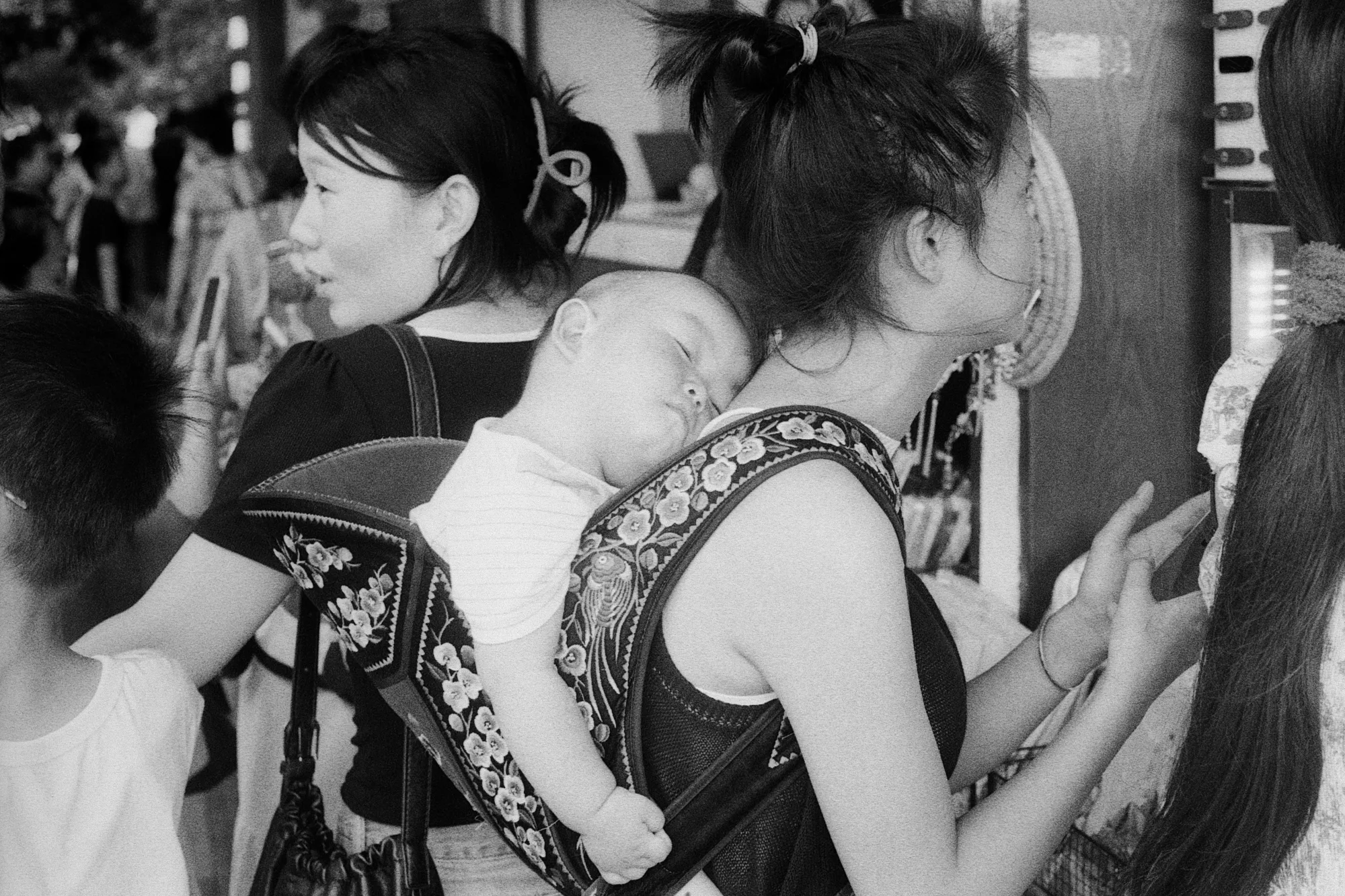A sleeping child rests against an adult's shoulder in the middle of a crowd.